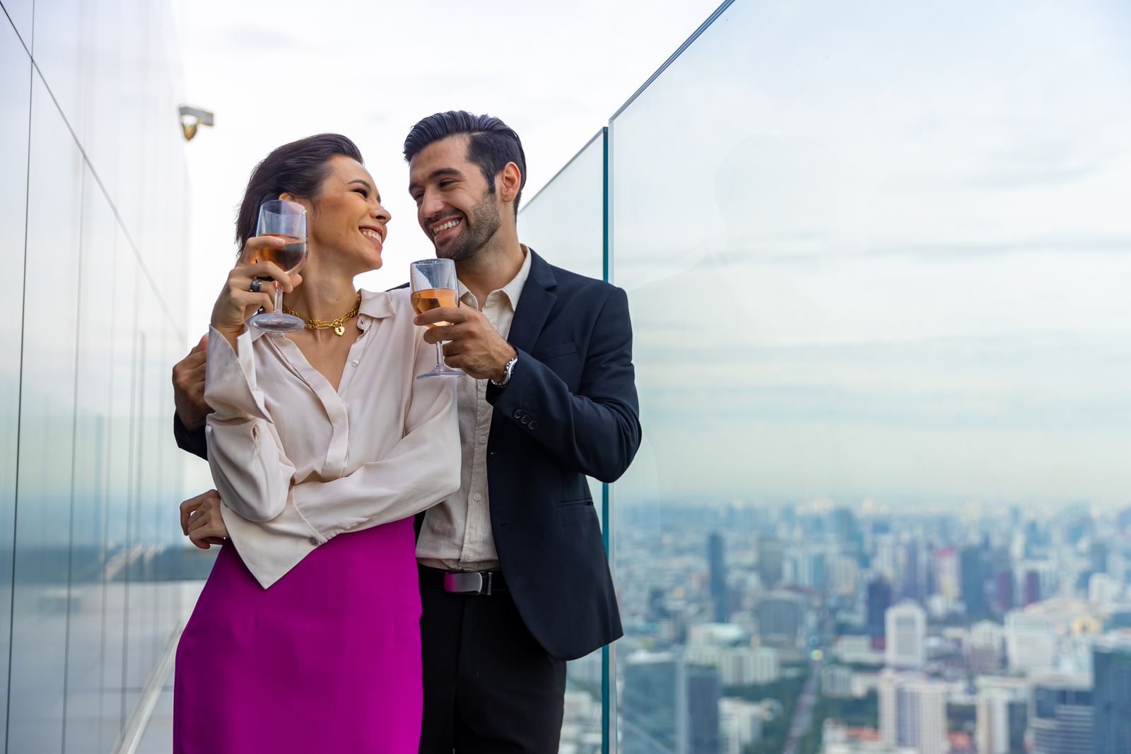 A couple at a rooftop bar against a sunset city skyline